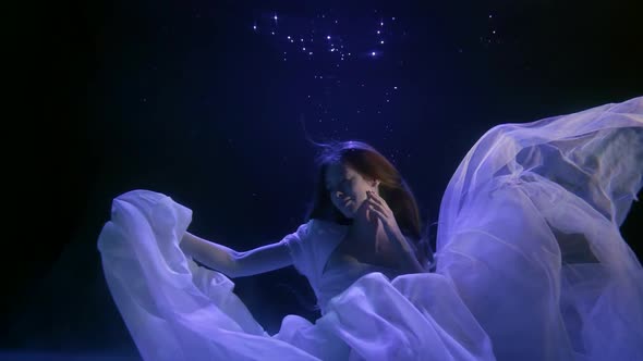 a Beautiful Girl in a White Dress Is Floating in the Dark Water. She Brushes Her Hair Away From Her