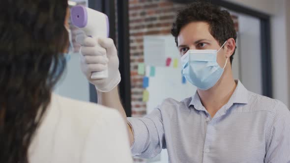 Man wearing face mask checking temperature of woman at office