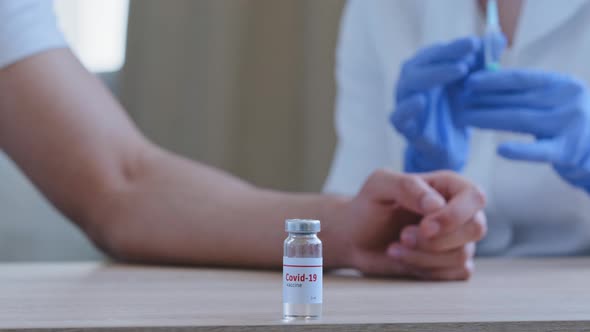 Closeup Bottle with Covid19 Vaccine Stands on Table in Hospital Female Doctor Hands Hold Syringe