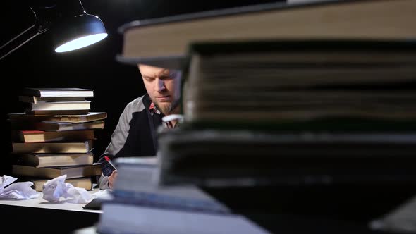 Man Sitting at the Table Nervously Crumples Sheets. Black Background