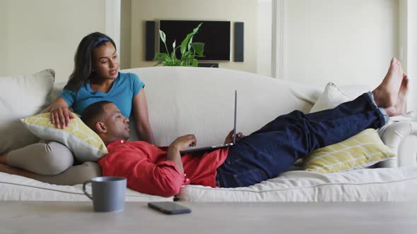 Happy biracial couple on sofa with laptop and talking