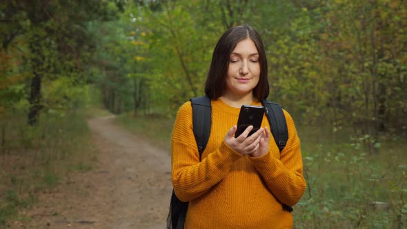 Woman Hiker Texts on Mobile Phone Standing in Green Forest