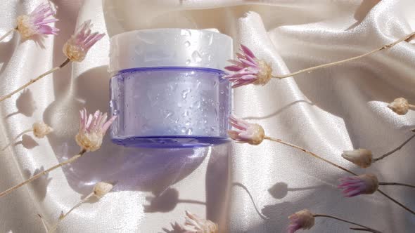 Blue glass cream jar mockup on smooth silk fabric sunlight flowers shadow water splashes Skincare 4K