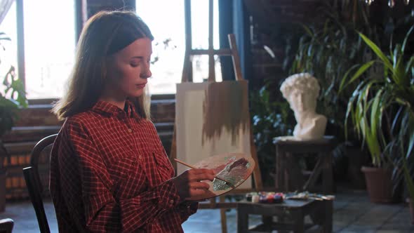 A Young Woman Artist Mixing Colors on a Wooden Palette and Looking in the Camera