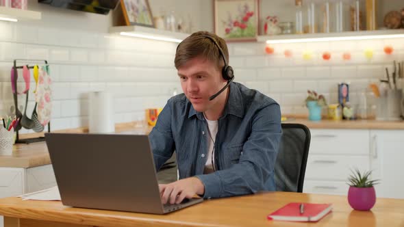 Male Gamer wearing Headphones, playing a Video Game on his Laptop PC in kitchen at home.