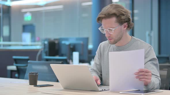 Businessman with Laptop Reading Documents in Office