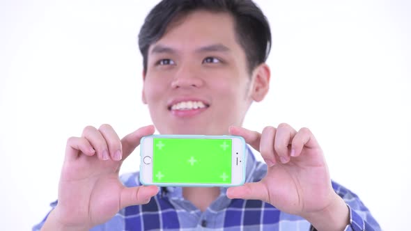 Face of Happy Young Asian Hipster Man Thinking While Showing Phone