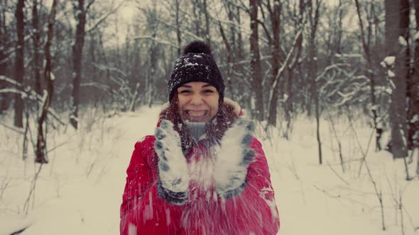 Young Woman in Hat and Gloves Throws Snow Standing in Forest