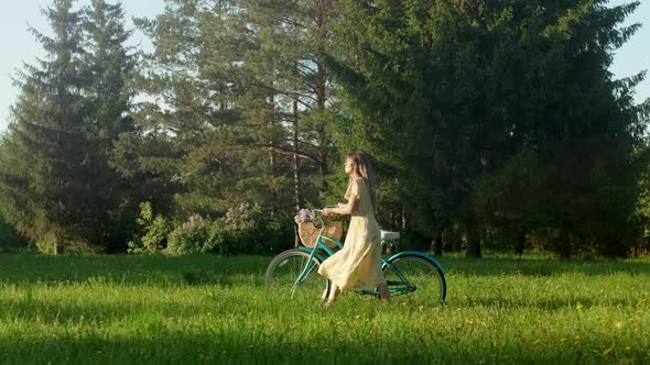 Happy Young Woman Walk With a Bike With Basket of Flowers on the On Countryside Road At Summer at