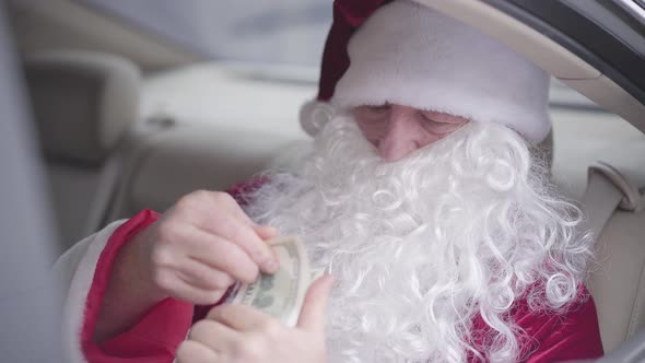 Old Santa Claus Sitting in the Car on Back Seat Sniffing Pack of Dollars and Smiling, Then He Raises