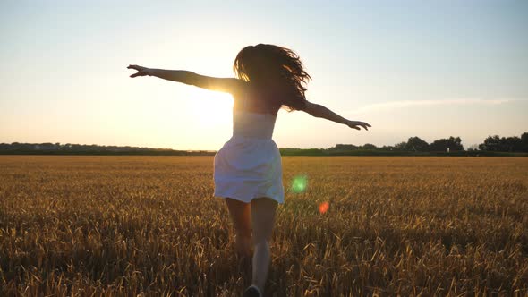 Attractive Joyful Woman in White Dress Running Through Field of Wheat at Sunset