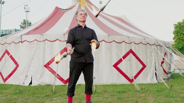 Male circus acrobat juggling with burning clubs