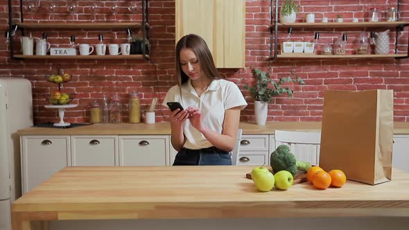 Woman Browsing on Mobile Phone at Home Kitchen. Young Woman Browsing on Smartphone Smiling Happy.