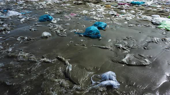 Sandy ocean coastline covered in piles of plastic while young beautiful woman walking