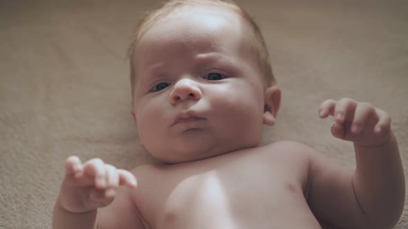 Infant Boy with Large Blue Eyes and Cheeks Lies on Table