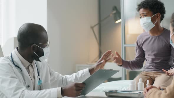 Black Pediatrician in Mask Speaking with Boy and His Mother in Medical Office