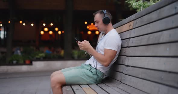 Man Listening to Music in Headphones Sitting on Bench