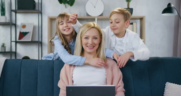 Mother with Computer on the Couch and Looking at Camera with Her Two Teen Kids