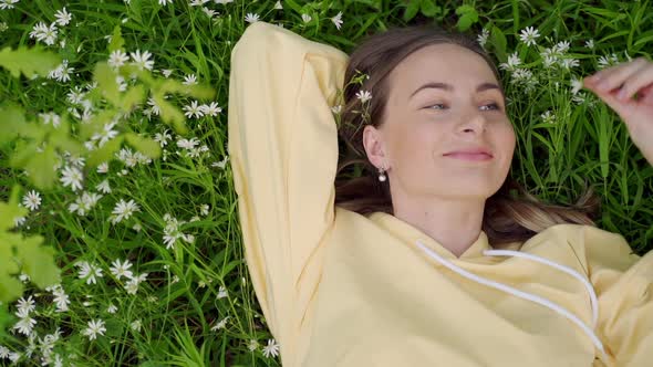 Beautiful Young Woman Lying on the Grass Against the Background of Flowers in the Forest