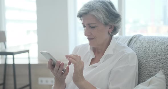 Smiling Senior Woman Staring at Smartphone Screen While Viewing Amusing Photo or Video