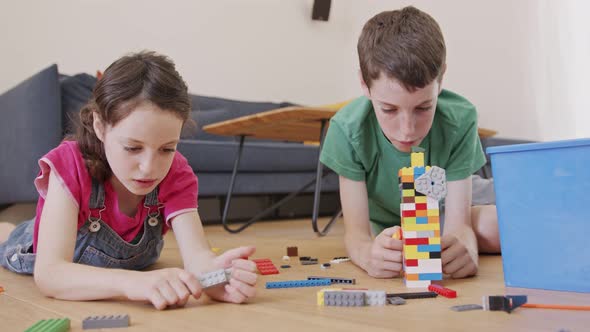 Girl and a boy playing and constructing with toy bricks on the living room floor