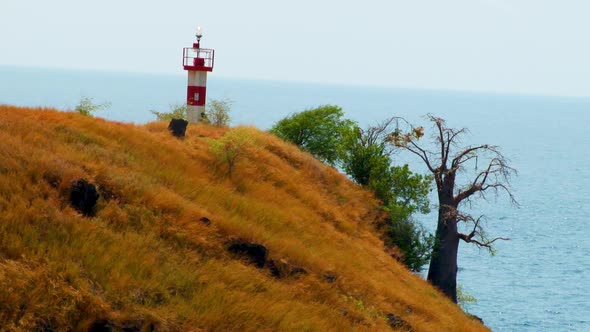 A small lighthouse sits on a small cliff overlooking the ocean along a coast in Africa