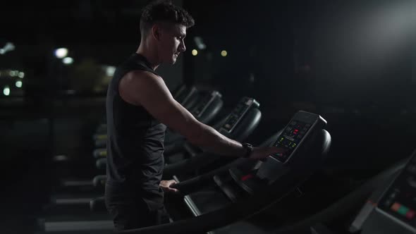 Cinematic Lighting Athletic Man Starts Jogging Run on a Treadmill Aerobic Exercise and Endurance