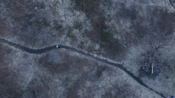 A top down view directly above two people walking on a dirt path in a park during a cloudy evening.