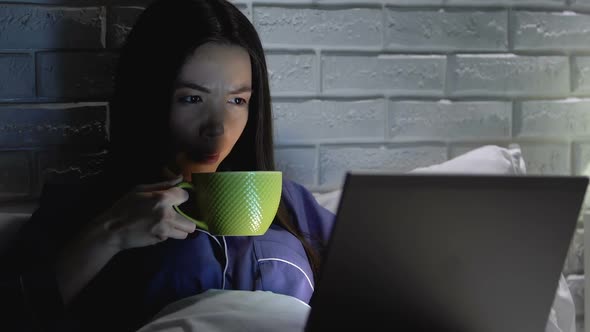 Tired Woman Drinking Hot Tea and Working on Laptop in Bed at Night, Deadline