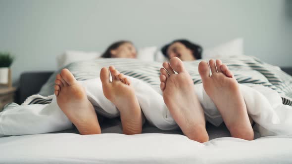 Bare Feet Male and Female Moving in Bed Under Blanket in Funny Dance