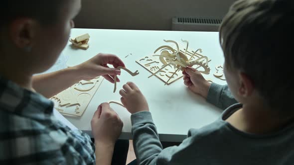 Mom helps her son to make a wooden toy according to the instructions