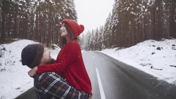 Young Couple in Love Kiss in First Snowy Winter Day in Forest Outdoors. Man and Girl on Date Meeting