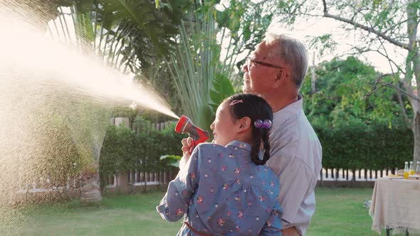 Retirement Grandfather and granddaughter watering the plants at the home garden.