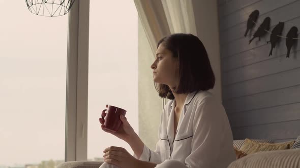 Attractive Girl Looks Out the Window at Cosy Flat