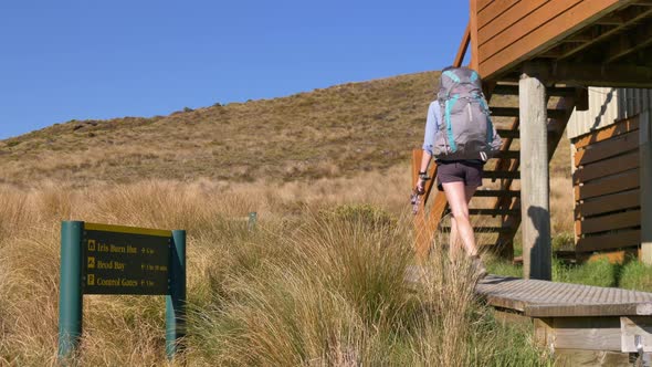 Static, hiker leaves Luxmore Hut past sign, Kepler Track New Zealand