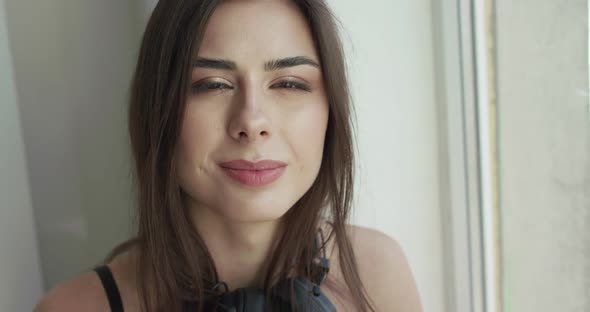 Portrait of Happy Girl Touches Headphones on Neck, Looks and Smiles at Camera