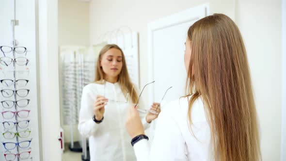 Woman in optic store choosing glasses. Beautiful girl wearing glasses in optician shop