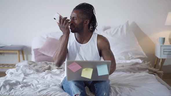 Portrait of Serious African American Man Surfing Internet on Laptop and Recording Voice Message on