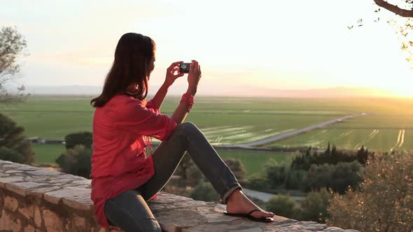 Young woman sitting on wall with camera