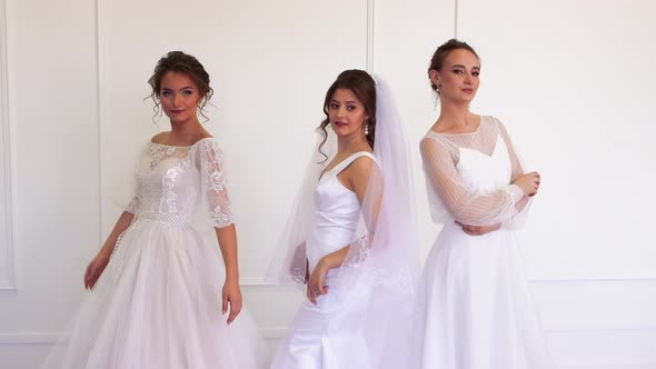 Three Girls in Wedding Dresses are Posing Coquettishly