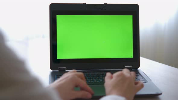 A nurse in a bathrobe is typing on a laptop with a green screen on the table