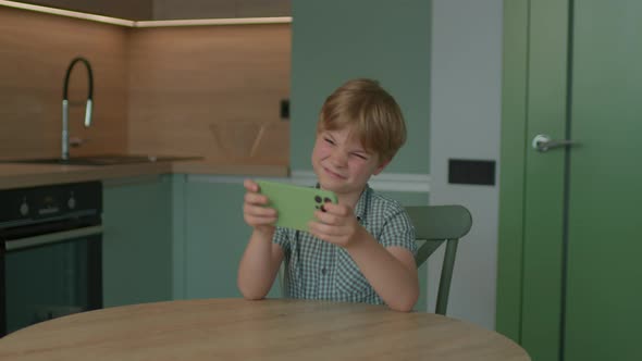 School Child Playing Video Game Using Mobile Phone Sitting in the Kitchen