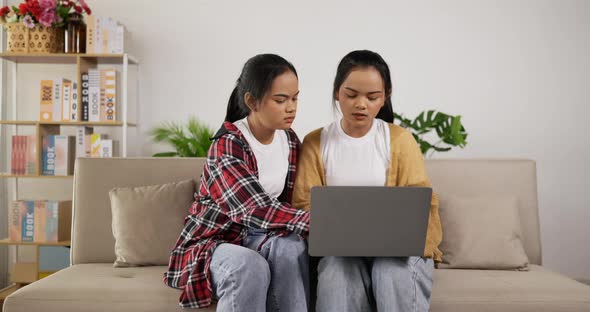 Twin girls planning for work to laptop while sitting on couch