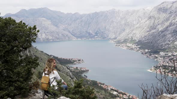 A Girl with a Backpack Sits on Top of a Mountain in Montenegro