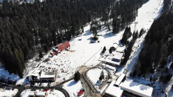 Aerial view of the bottom of the ski slope at Poiana Brasov panning up to reveal the slope