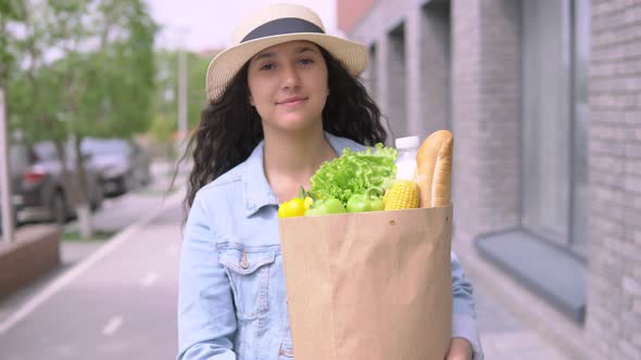 Young Beautiful Woman in a Denim Jacket and Hat Carries a Grocery Bag