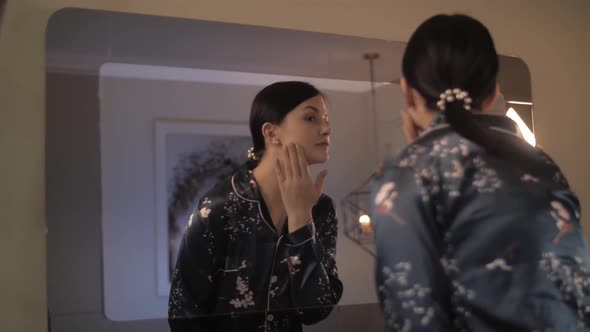 Happy Young Woman Putting Cream on Face Smiling Looking at Mirror