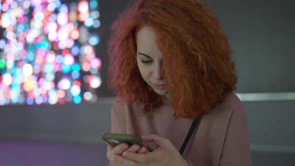 A girl with red hair looks at her smartphone while doing something