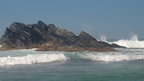 Heavy Ocean Waves Beat Against Large Dark Brown Rocky Stones