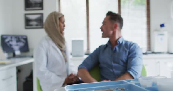 Biracial female dentist talking with male patient at modern dental clinic